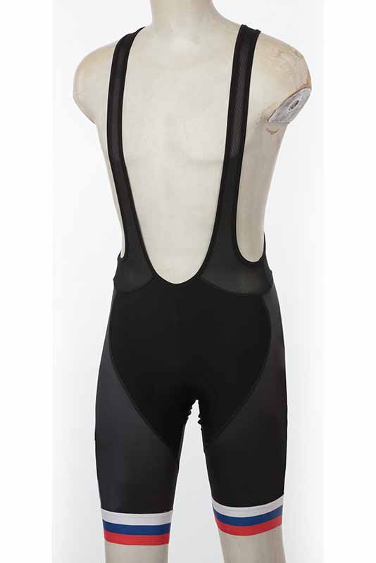 A ghost mannequin service showcases black cycling bib shorts with shoulder straps on a white, faceless form. The shorts are adorned with horizontal red, white, and blue stripes wrapping around each leg near the hem.