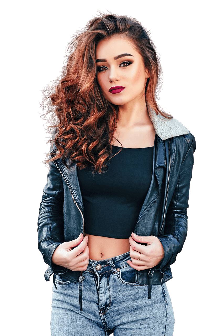 A woman with long, wavy brown hair stands confidently, wearing a black crop top, a black leather jacket with a shearling collar, and blue jeans. She has bold makeup and is holding the edges of her jacket with both hands. The background is transparent, perfect for showcasing our photo retouching services.