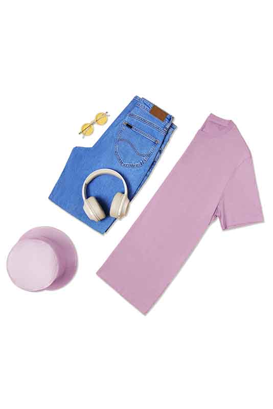 Flat lay of casual outfit: folded blue jeans with brown leather patch, light purple t-shirt, light purple bucket hat, beige over-ear headphones, and yellow-tinted round sunglasses, after edit.