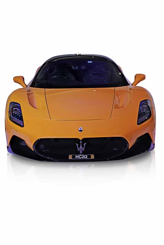 A yellow Maserati MC20 sports car after edit is showcased in a well-lit showroom, with its sleek and aerodynamic design prominently displayed. The car's front view highlights its bold grille and iconic trident logo.